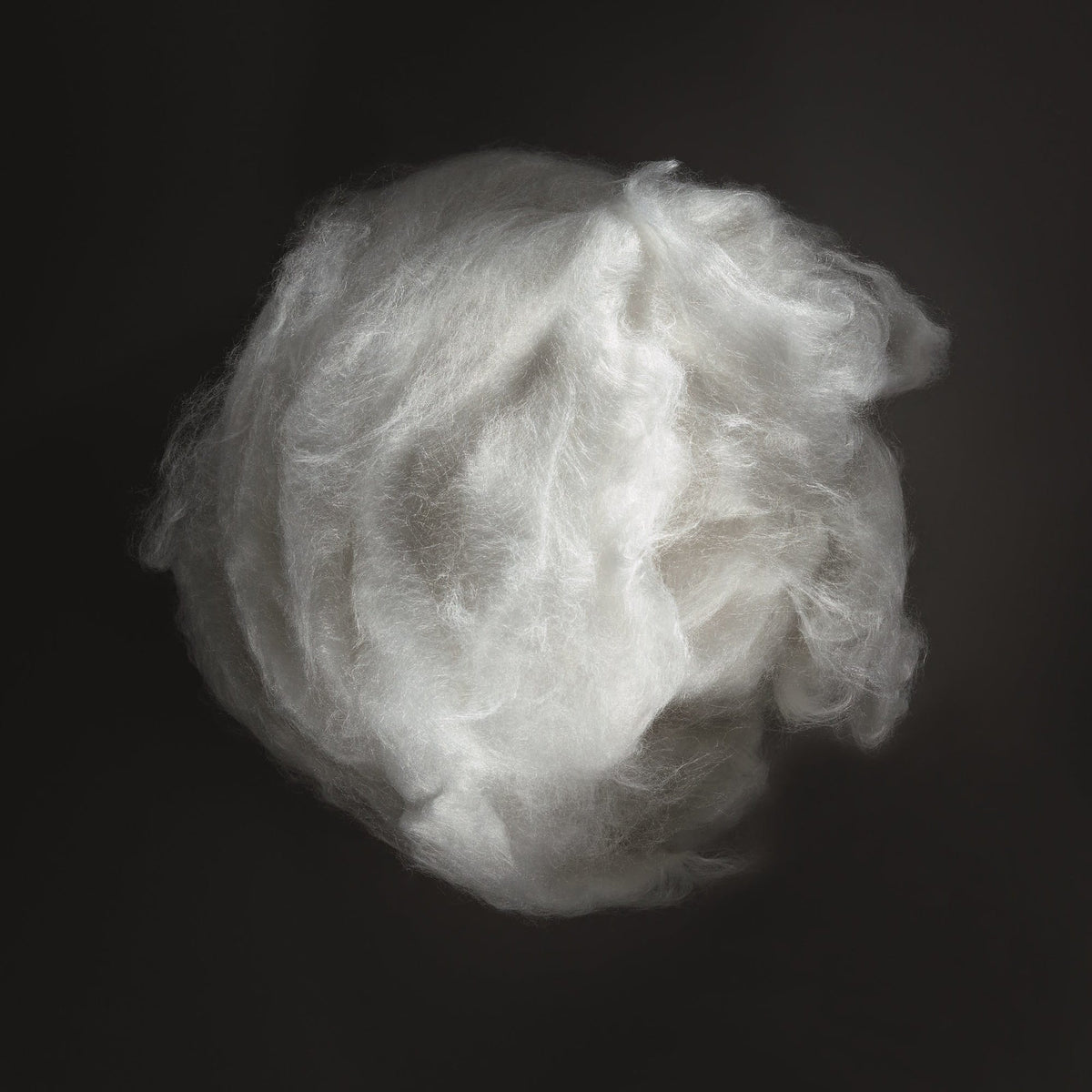 A ball of fluffy white cotton batting or fiber, photographed against a solid black background.