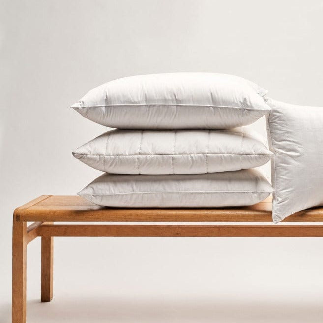 Stack of pillows on a wooden bench against a light gray background