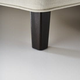 Close-up of a dark wooden leg on a light-colored sofa.