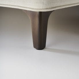 Close-up of a dark wooden leg of a piece of furniture on a light gray background
