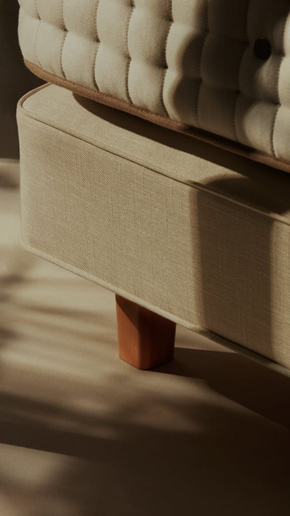 Close-up of a beige upholstered ottoman with wooden legs on a wooden floor.